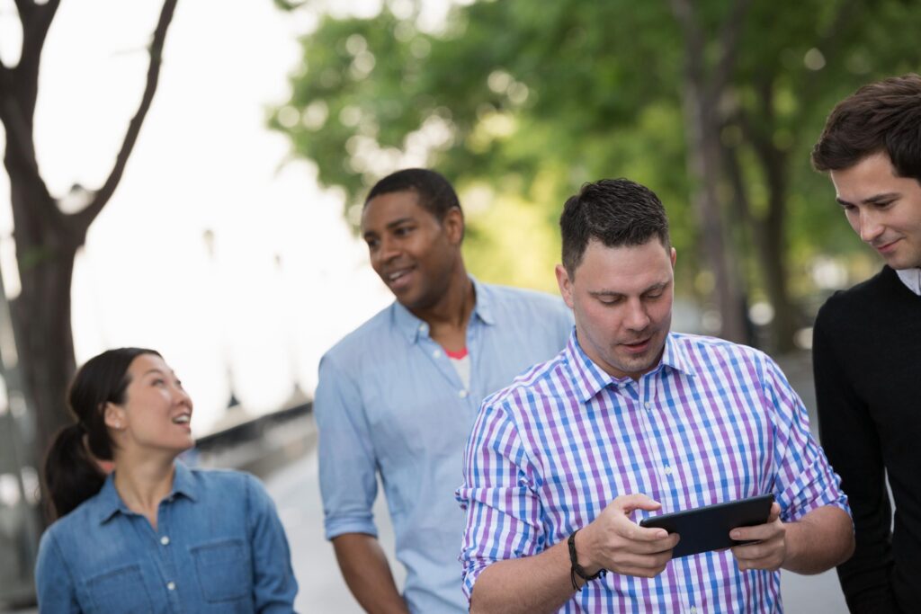 A group of four colleagues walking together outdoors, with one person using a tablet, symbolizing teamwork and the use of technology during a team-building activity.