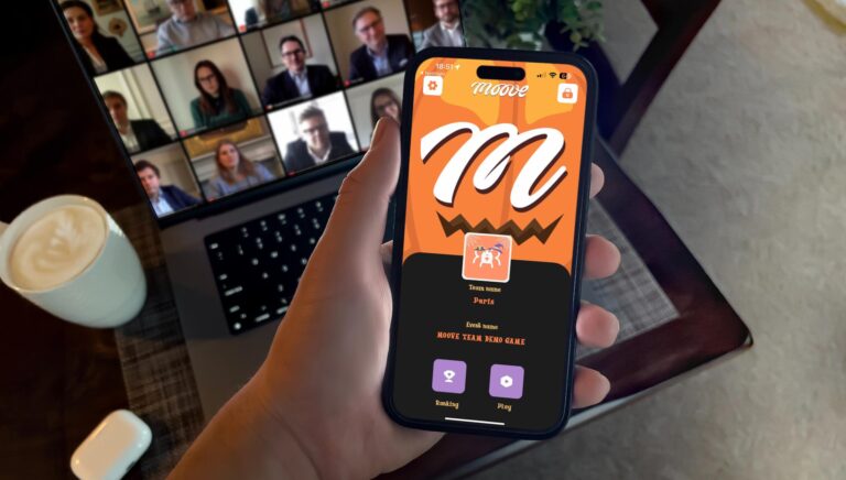 Person holding a smartphone displaying the MooveXR Halloween-themed app screen, featuring a festive orange and black design with a pumpkin motif. In the background, a video call with colleagues on a laptop and a cup of coffee can be seen.