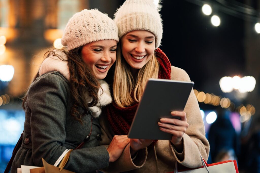 Mujeres disfrutando de un evento al aire libre en una noche navideña con luces festivas de fondo.