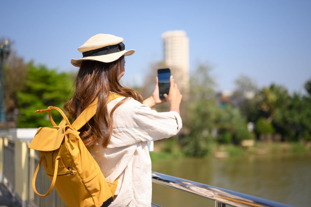 A tourist woman using her smartphone to access a self-guided MooveGOXR experience near a river, demonstrating autonomous activation without staff.