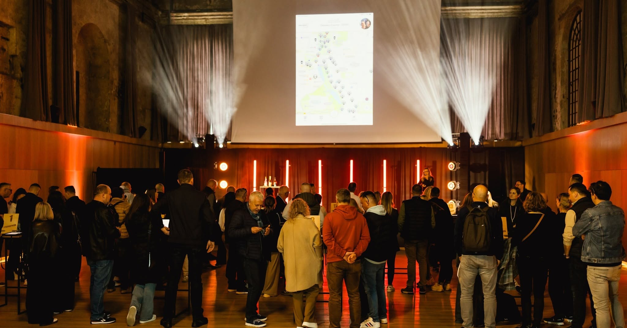 Event attendees observing a large projected gamified map during a corporate gathering.