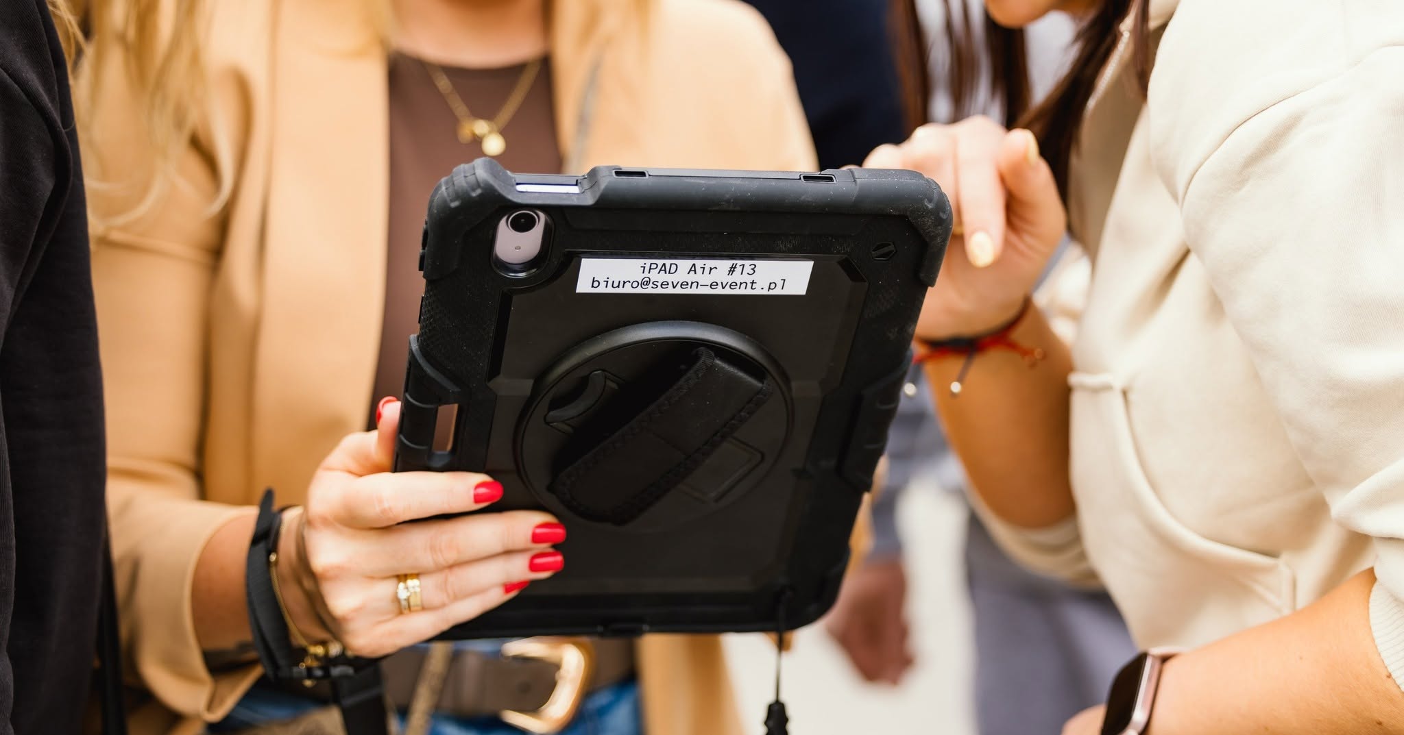 Five participants gathered around a rugged iPad Air in a protective case during a corporate team-building activity, using the tablet to complete interactive gamification challenges